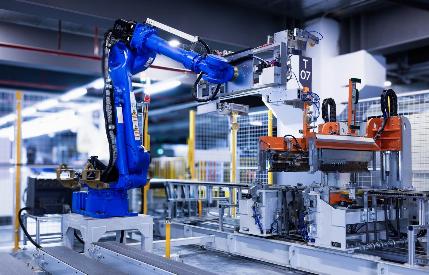 Six-axis industrial robotic arm with custom end effector integrated into a manufacturing workcell with conveyor and controller electronics