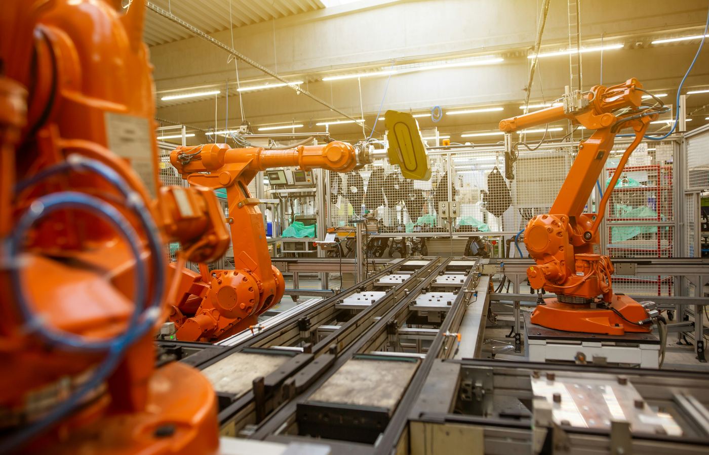 Six-axis industrial robotic arms with end-of-arm tooling positioned along a conveyor-fed manufacturing line